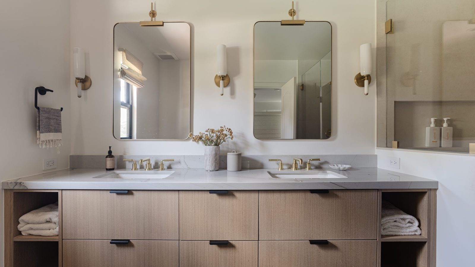 Serene double vanity bathroom with a quartz countertop, rift oak cabinetry, brass fixtures, and paired arched mirrors