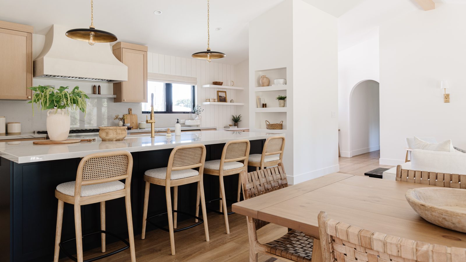 Open-plan kitchen with white oak cabinetry, a deep navy island, brass pendant lights, and an adjoining dining table