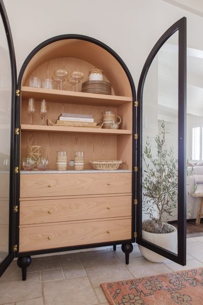 Tall arched display cabinet with a black metal frame and oak shelving, holding glassware and ceramics