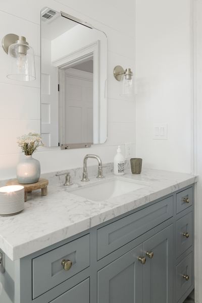 Bathroom vanity in soft blue-grey with a marble countertop, brass fittings and a slim framed mirror