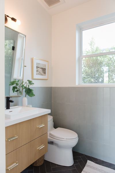 Bathroom with a floating white oak vanity, sage green tiled wainscot, black fixtures and a window above