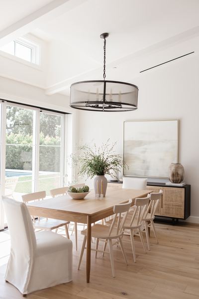 Dining room with an oak table, mixed slipcovered and spindle chairs, a black drum chandelier and large garden windows