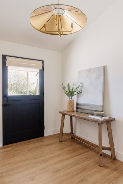 Entry hall with a black Dutch door, brass pendant, slim wood console table and wide-plank oak floors