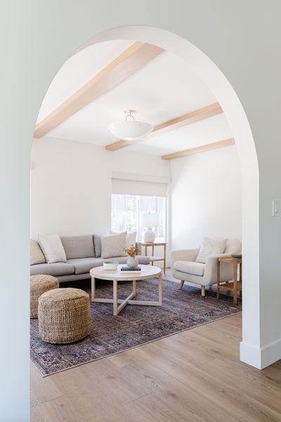 Great room viewed through a plaster archway, with exposed beams, neutral seating and a vintage patterned rug