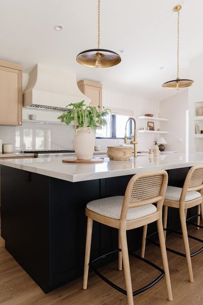 Kitchen island in deep navy with a white quartz top, cane-back counter stools and two brass dome pendants