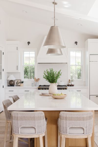 Kitchen with a long white island, woven counter stools, a plaster range hood and a skylight overhead
