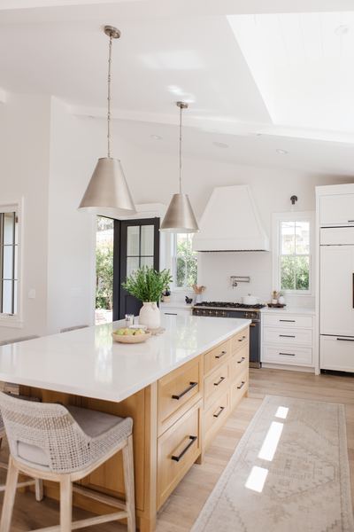Kitchen with a white oak island, two white cone pendants, marble countertops and a polished stone floor