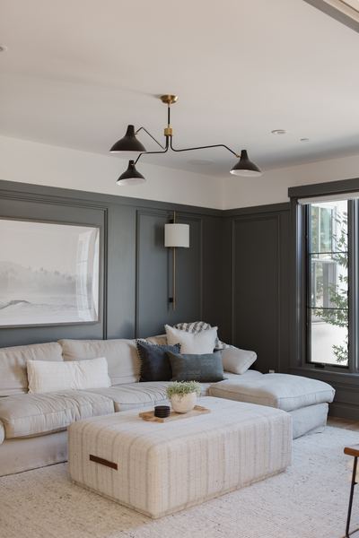 Living room with deep charcoal walls, a cream sectional, upholstered ottoman and a black linear chandelier