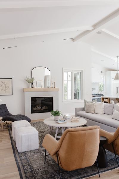 Living room with a white fireplace surround, arched mirror above the mantel, tan leather chairs and a vintage rug