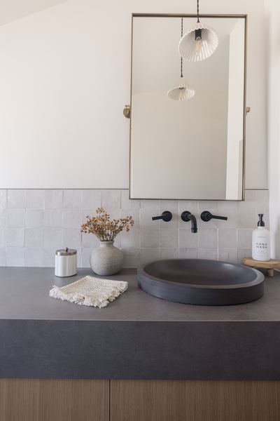 Powder room vanity with a dark stone countertop, carved stone vessel sink, black wall-mounted faucet and a large brass-framed mirror
