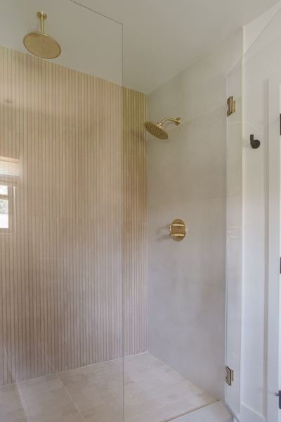 Walk-in shower lined with fluted vertical tile, brass shower fittings and a glass panel
