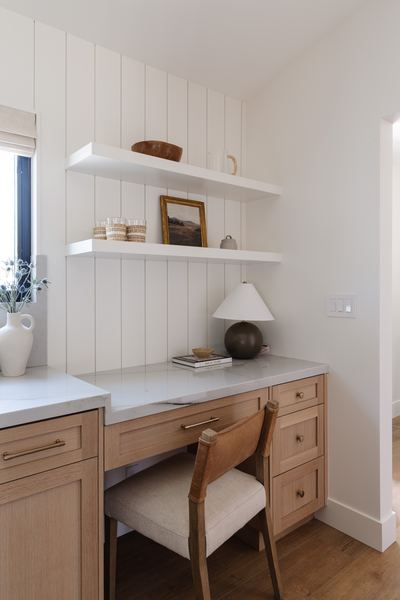 Built-in study nook with oak cabinetry, floating shelves, a table lamp and a cane-back chair against vertical shiplap