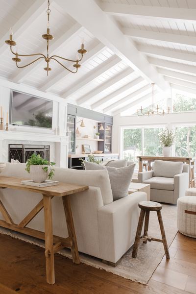 Sunroom with vaulted white-painted beams, skylights, brass chandeliers, a console table and pale upholstered seating