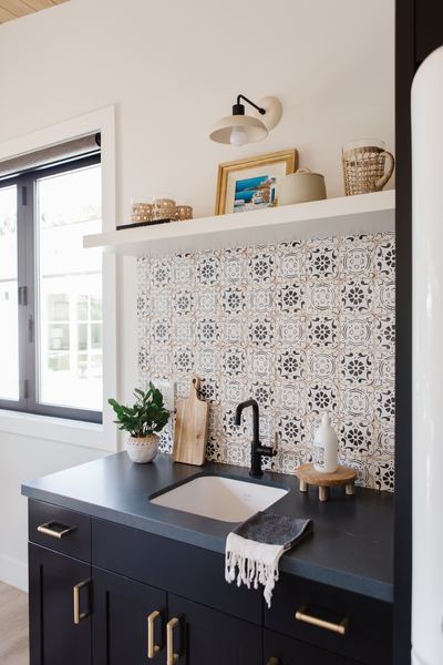 Vanity with black cabinetry, patterned cement tile backsplash, brass hardware and a picture light above open shelving