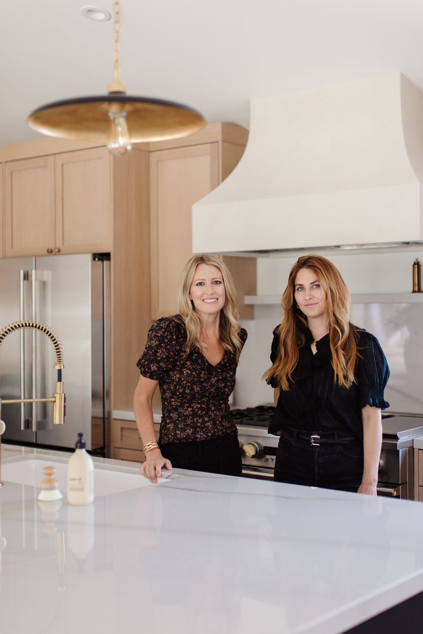 The Flourish Home Studio design team in a completed kitchen with white oak cabinetry, a plaster range hood, and a brass pendant light